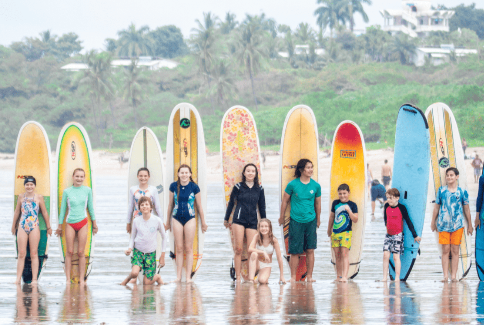 group of Prisma students holding surfboards on a tropical beach with palm trees